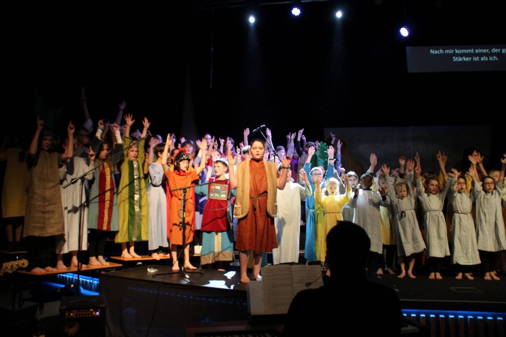 65 Schülerinnen und Schüler aus FES-Gymnasium und FES-Realschule brachten das biblische Musical "Johannes der Täufer" auf die Bühne des großen Saals der Brückengemeinde HDH. Die Produktion des 6. Klassen unserer Schule begeisterte mit eingängiger Musik, farbenfroher Inszenierung und klarer Botschaft.