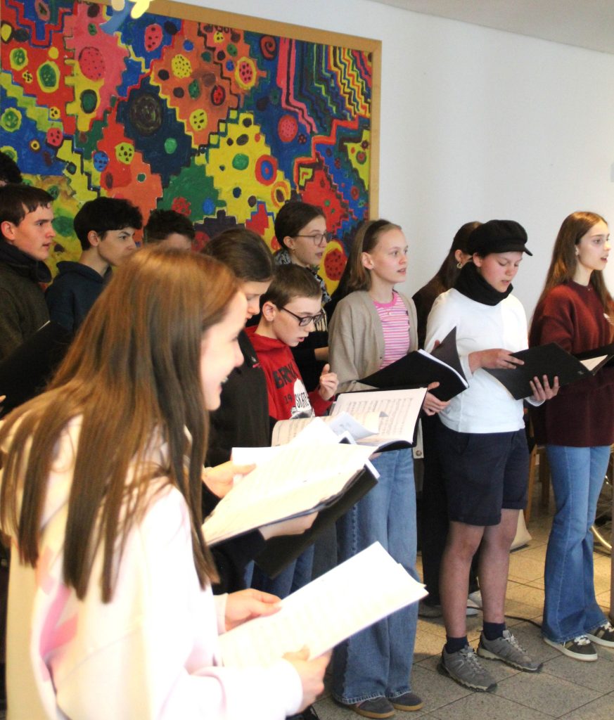 BLOG-Beitrag
FES-Schüler überraschen Bewohner im Altenzentrum musikalisch
Tränen der Rührung, Glück und Freude: So viele gute Gefühle in einem Gesicht ablesen zu können, ist wohl der beste Beweis für eine gelungene Aktion.                                                          
20 Schülerinnen und Schüler unseres FES-Jugendchors blickten bei ihrem kleinen musikalischen Ständchen im Eugen-Lederer-Altenzentrum in HDH am Mittwoch in ganz viele glückliche Gesichter: Die Schüler unseres FES-Gymnasiums und unserer FES-Realschule besuchten mit FES-Chorleiter Daniel Kindsvater und Schulleiter Andreas Borkeloh die Senioren im AWO-Altenzentrum in der Stadtmitte und überraschten mit europäischer Chormusik unterschiedlicher Stilistik aus dem aktuellen Konzertprogramm. Die Cafeteria war beim Besuch der jungen Sänger aus den Klassenstufen 7-10 proppenvoll gefüllt und die jungen Choristen erfüllten das Auditorium mit fröhlicher Musik. Besondere Freude bereitete den älteren Menschen, dass zum Abschluss des musikalischen Ständchens gemeinsam gesungen wurde. „Vielen Dank, dass Ihr heute bei uns seid. Unsere Bewohner freuen sich riesig, dass ihr für sie singt“, bedankte sich Nadine Schnell, Pflegedienstleitung im AWO-Altenzentrum am Ende des gut 30-minütigen kleinen chorischen Vortragsprogramms.

